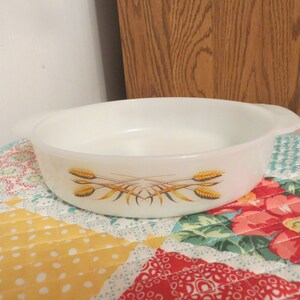 May include: White glass baking dish with a design of wheat stalks in yellow and brown. The dish has two handles.