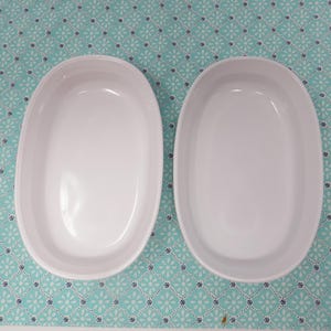 May include: Two white oval ceramic baking dishes on a turquoise background with a white floral pattern.