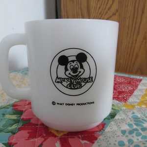 Pode incluir: Caneca de cer&acirc;mica branca com um logotipo do Mickey Mouse Club em preto e branco. O logotipo apresenta a cabe&ccedil;a do Mickey Mouse com um c&iacute;rculo ao redor e o texto "Mickey Mouse Club". A parte inferior da caneca diz "&copy; Walt Disney Productions".