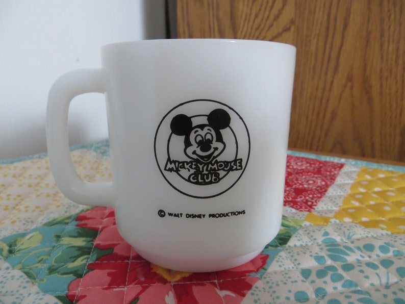 Pode incluir: Caneca de cer&acirc;mica branca com um logotipo do Mickey Mouse Club em preto e branco. O logotipo apresenta a cabe&ccedil;a do Mickey Mouse com um c&iacute;rculo ao redor e o texto "Mickey Mouse Club". A parte inferior da caneca diz "&copy; Walt Disney Productions".