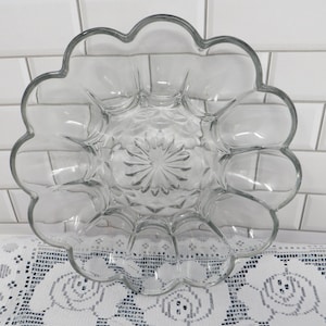 May include: A clear glass serving dish with a scalloped edge and a flower-shaped center design. The dish features twelve individual rounded compartments arranged in a circular pattern, radiating from a central starburst motif in the glass.