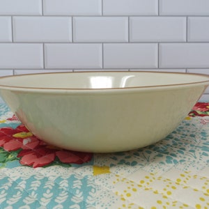 May include: A large, off-white ceramic mixing bowl with a brown rim. The bowl is sitting on a colorful quilted fabric.