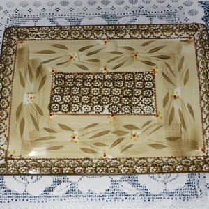 May include: A rectangular ceramic serving tray with handles, featuring a cream-colored center with brown painted leaf motifs and small red and yellow dots. The border is decorated with a dense, repeating brown and white floral pattern.