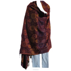 May include: A maroon shawl with a paisley pattern in shades of purple, orange, and yellow. The shawl is draped over a mannequin and has fringe on the bottom.