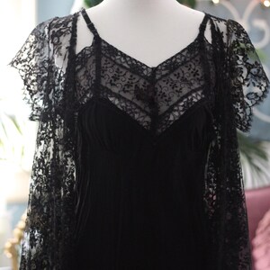 K&ouml;nnte beinhalten: Schwarzes Lingerie-Set im Vintage-Stil auf einer Schaufensterpuppe. Das Set umfasst ein Slip-Kleid mit V-Ausschnitt und zarter Spitze sowie einen passenden Spitzen-Overlay mit kurzen &Auml;rmeln. Das Design ist elegant und romantisch, mit aufwendigen Details.