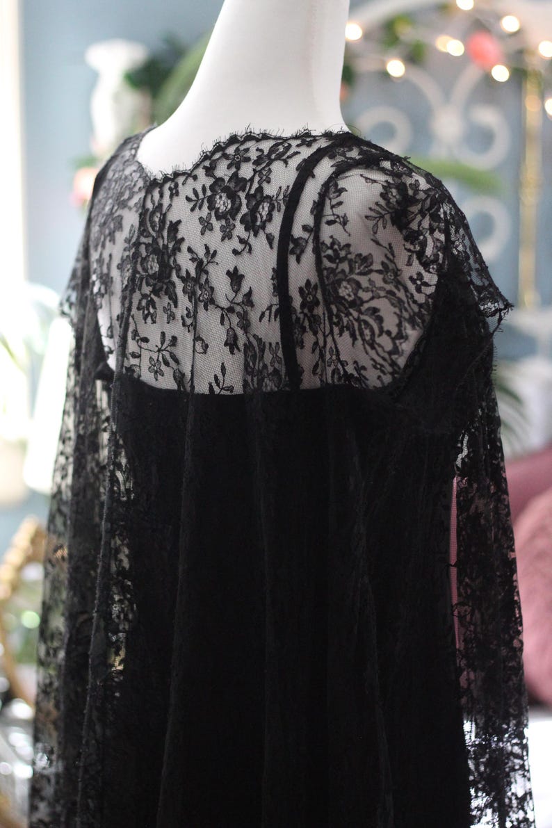 K&ouml;nnte beinhalten: Schwarzes Spitzentop mit floralen Mustern, auf einer Schaufensterpuppe pr&auml;sentiert. Das Top hat eine transparente Spitzenauflage &uuml;ber einem einfarbigen schwarzen Stoff, mit einem gewellten Rand am Ausschnitt und an den &Auml;rmeln. Das detaillierte Spitzendesign verleiht Eleganz.