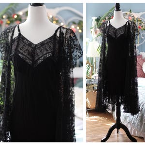 K&ouml;nnte beinhalten: Ein schwarzes Kleid im Vintage-Stil mit einer zarten Spitzenauflage und einem passenden Spitzenumhang. Das Kleid hat einen V-Ausschnitt und Spaghettitr&auml;ger. Der Umhang hat kurze &Auml;rmel und aufwendige Blumenmuster.
