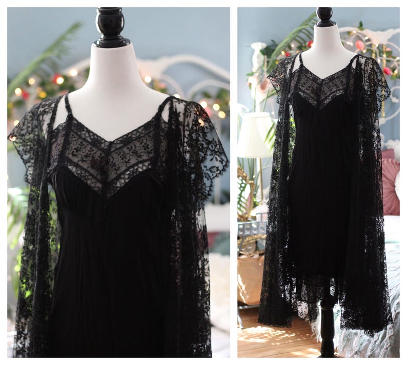 K&ouml;nnte beinhalten: Ein schwarzes Kleid mit V-Ausschnitt und zarten Spitzendetails. Das Kleid wird mit einem passenden Spitzenumhang kombiniert, wodurch eine elegante und gotische &Auml;sthetik entsteht. Das Kleid wird auf einer Schaufensterpuppe pr&auml;sentiert.