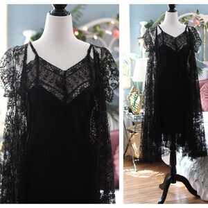K&ouml;nnte beinhalten: Schwarzes Spitzenkleid mit V-Ausschnitt und Spaghettitr&auml;gern. Das Kleid wird mit einem passenden Spitzenumhang mit kurzen &Auml;rmeln kombiniert. Das Kleid wird auf einer Schaufensterpuppe pr&auml;sentiert.
