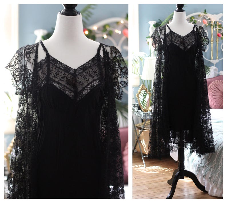 K&ouml;nnte beinhalten: Schwarzes Spitzenkleid mit V-Ausschnitt und Spaghettitr&auml;gern. Das Kleid wird mit einem passenden Spitzenumhang mit kurzen &Auml;rmeln kombiniert. Das Kleid wird auf einer Schaufensterpuppe pr&auml;sentiert.
