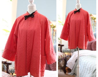 May include: A coral pink quilted jacket with a black velvet bow at the collar. The jacket has long sleeves with wide cuffs and two patch pockets.