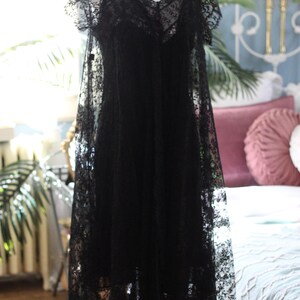 K&ouml;nnte beinhalten: Schwarzes Spitzenkleid auf einer Schaufensterpuppe. Das Kleid hat einen V-Ausschnitt, kurze &Auml;rmel und einen flie&szlig;enden Rock. Die filigrane Spitze bedeckt das gesamte Kleid und erzeugt ein zartes und elegantes Aussehen. Das Kleid ist bodenlang.