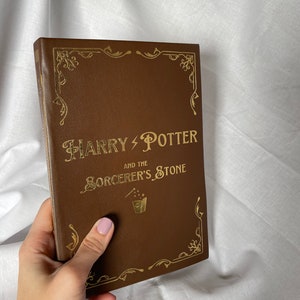 May include: A brown leather-bound book with gold lettering that reads "HARRY POTTER AND THE SORCERER'S STONE".