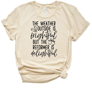 May include: A beige t-shirt with black text that reads "The weather outside is frightful but the reformer is delightful". The text is decorated with holly and jingle bells.