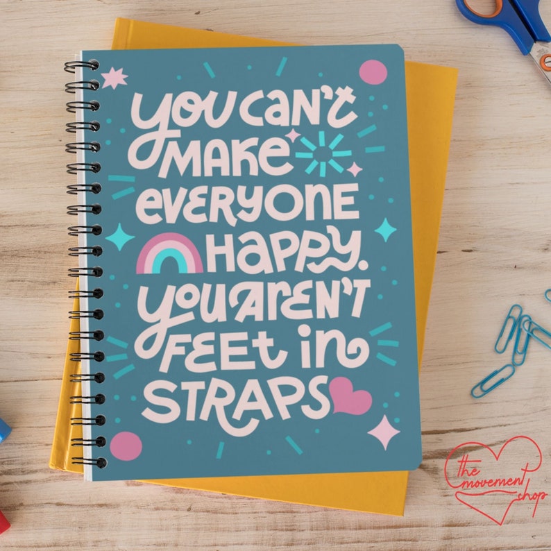 May include: A blue spiral notebook with the text "You can't make everyone happy. You aren't feet in straps." The text is in a colorful, handwritten style with a rainbow and a pink heart.