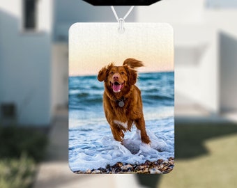 May include: A brown and white dog runs through the waves on a beach. The dog is wearing a black collar with a silver tag. The image is a car air freshener.