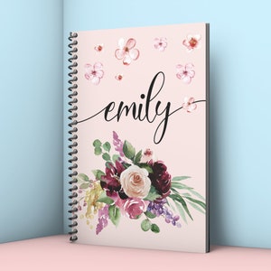 May include: A pink spiral notebook with a floral design and the name "emily" written in black cursive. The flowers are a mix of burgundy, pink, and white.