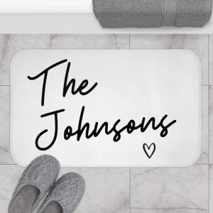 May include: White bath mat with black text that reads "The Johnsons" with a small heart symbol.