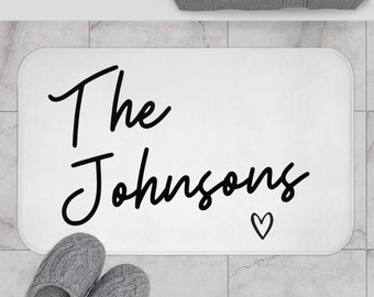 Może przedstawiać: Biała mata łazienkowa z czarnym tekstem, który brzmi "The Johnsons" z małym symbolem serca.