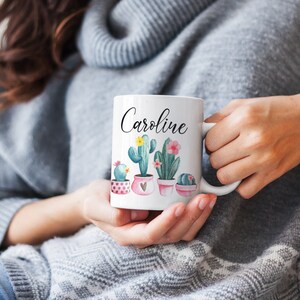 May include: White ceramic mug with a pink, green, and yellow cactus design. The mug has the name "Caroline" written on it in black.