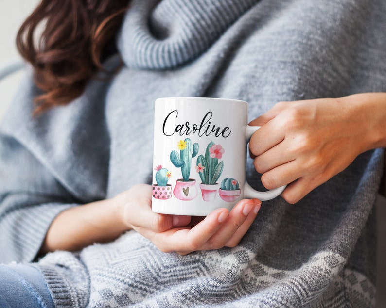 May include: White ceramic mug with a pink, green, and yellow cactus design. The mug has the name "Caroline" written on it in black.