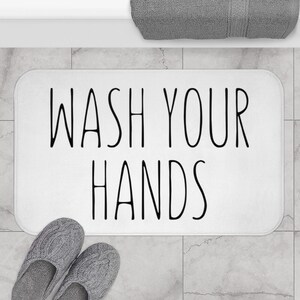 May include: White bath mat with black text that reads "WASH YOUR HANDS".