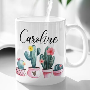 May include: White ceramic mug with a black cursive name "Caroline" and a watercolor design of five potted cacti with pink and yellow flowers.