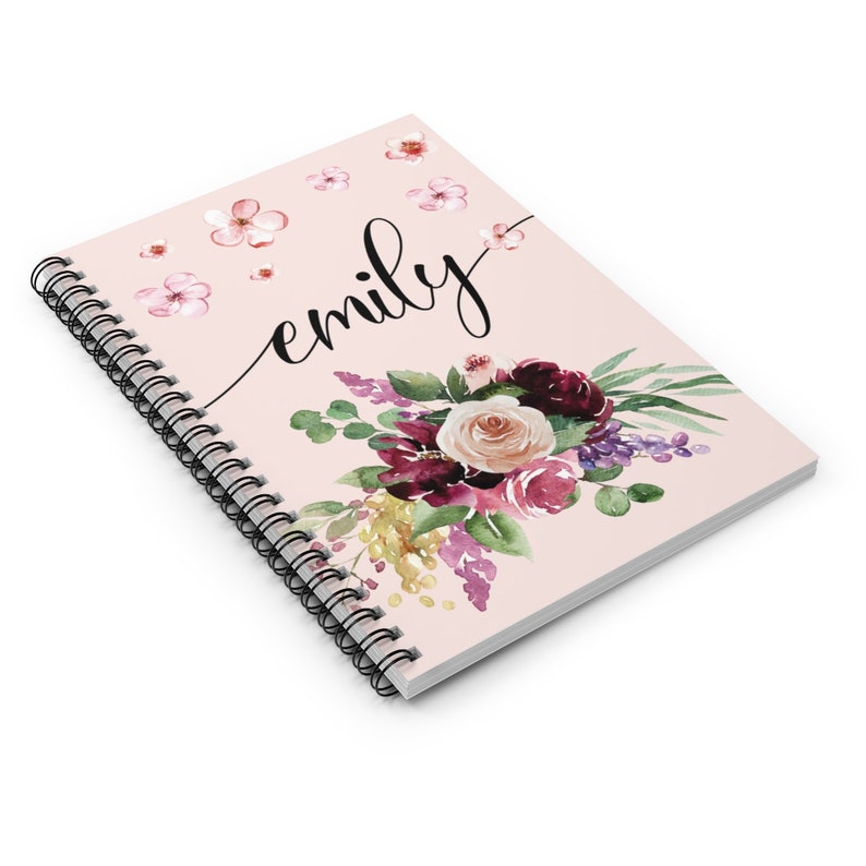 May include: A pink spiral bound notebook with a floral design and the name "emily" written in cursive. The flowers are in shades of pink, purple, and burgundy.
