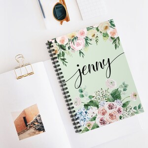 May include: A green spiral notebook with a floral design and the name "jenny" written in black cursive. The flowers are pink, white, and blue.