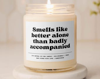 May include: A white candle with a black label that reads "Smells like better alone than badly accompanied". The candle is lit and sitting on a white marble coaster.