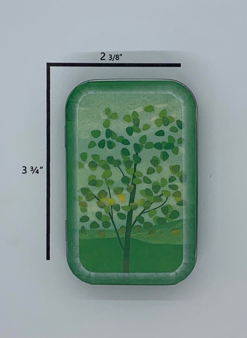 May include: A green metal tin with a rounded rectangular shape. The tin features a design of a green tree with yellow leaves against a light blue sky. The tin measures 2 3/8 inches by 3 3/4 inches.