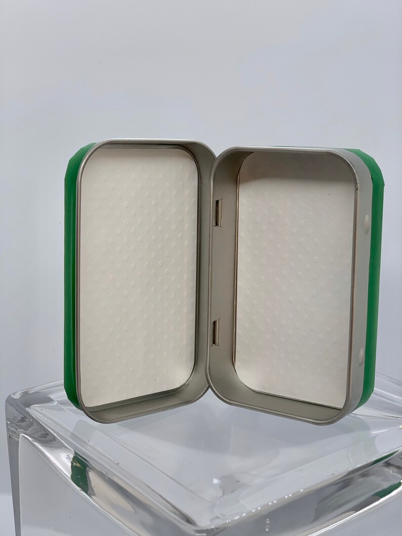May include: A green and silver metal box with a white foam interior. The box is open and the foam is visible.