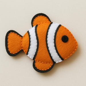 May include: A handmade felt fish in orange, white, and black. The fish has a round black eye and is stitched with orange thread. The design resembles a clownfish, a popular marine animal.
