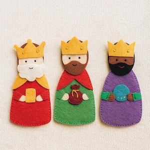 May include: Three felt figures of the Three Wise Men, each with a gold crown. The figures are in red, green, and purple robes, with details like beards and gifts. A festive, handmade Christmas decoration.