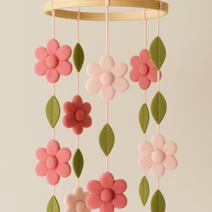 Pode incluir: Móbile de bebê com flores de feltro rosa e folhas verdes penduradas em um aro de madeira. As flores são em tons de rosa e as folhas são verde-claro. Decoração para o quarto do bebê.