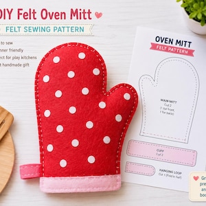 Puede incluir: Una manopla de horno de fieltro rojo con lunares blancos y un puño rosa claro, acompañada de una hoja de patrón de costura impresa etiquetada OVEN MITT FELT PATTERN con diagramas para la manopla, el puño y el lazo, y un juguete de cocina de madera.