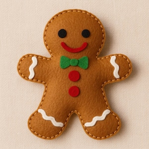 Pode incluir: Um boneco de gengibre de feltro castanho com um contorno costurado. Tem olhos pretos, um sorriso vermelho, uma gravata borboleta verde e dois botões vermelhos. Linhas onduladas brancas decoram os braços e as pernas. Uma decoração festiva de Natal.