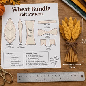 Pode incluir: Uma folha de instruções para um padrão de feltro Wheat Bundle com diagramas de corte e montagem, ao lado de um feixe de trigo de feltro acabado medindo 12 cm de altura por 6 cm de largura. Inclui uma régua de metal e tesouras douradas.