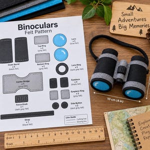 May include: A felt binoculars craft kit featuring a printed pattern sheet with assembly instructions, a finished black and gray felt binoculars toy with blue lenses, a wooden ruler showing 10 cm by 6 cm dimensions, and a sign reading Small Adventures Big Memories.