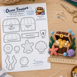 May include: A felt craft pattern sheet titled Ocean Treasure featuring templates for a treasure chest, starfish, seashell, and seaweed. Next to it is a finished felt treasure chest ornament measuring 10 cm wide, with gold coins and pearls.