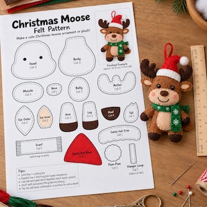May include: A Christmas Moose felt pattern sheet with printed templates for head, body, muzzle, nose, belly, antler, ear, arm, leg, hoof, tail, scarf, Santa hat, pom-pom, and hanger loop, alongside a finished felt moose ornament and a ruler.