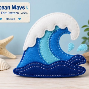 Puede incluir: Una pieza artesanal de fieltro con forma de ola oceánica, con tonos azules superpuestos, una cresta blanca y costuras blancas visibles. El diseño incluye dos pequeñas gotas de agua de fieltro azul claro a la derecha.