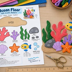May include: An Ocean Floor felt craft pattern sheet with instructions and templates for coral, fish, and shells. Beside it, finished felt pieces are assembled on a tan base, accompanied by embroidery floss, pins, scissors, and a ruler.