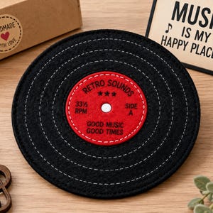 May include: A circular black felt coaster designed to resemble a vinyl record with white stitched circular grooves. The center label is red with white text reading RETRO SOUNDS, 33 1/3 RPM, SIDE A, and GOOD MUSIC GOOD TIMES with three stars.