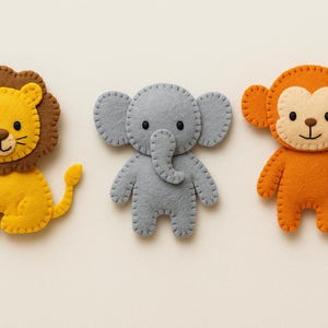 May include: Three felt animal figures: a yellow lion with a brown mane, a gray elephant, and an orange monkey. Each figure is hand-stitched with contrasting thread, featuring simple facial details. The lion has a tail, the monkey has a curled tail.