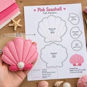 Puede incluir: Un proyecto de manualidades de fieltro rosa con forma de concha marina y una hoja de patrón impresa. La concha terminada mide 9 cm de ancho por 7,5 cm de alto. El patrón incluye piezas para el frente, la parte posterior y la perla, con líneas de costura.