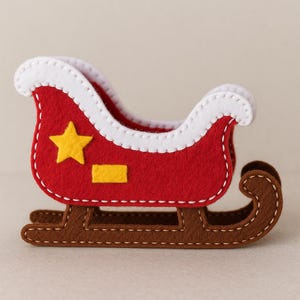 May include: A felt Christmas sleigh in red with white trim and a brown base. The sleigh features a yellow star and rectangle on the side. The sleigh is decorated with white stitching.