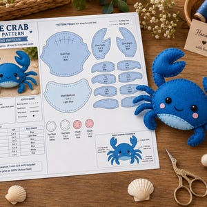 May include: A blue felt crab sewing pattern document featuring printed diagrams, a materials list, and assembly instructions. Beside the paper is a finished blue felt crab plush toy with pink cheeks, black eyes, and a light blue underbelly.