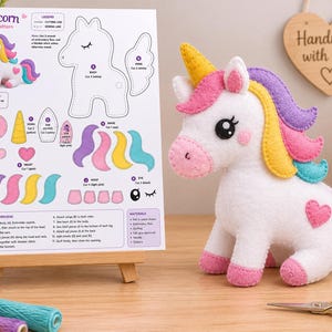 May include: A white felt unicorn plush toy with a yellow horn, pink cheeks, and a multi-colored mane and tail in purple, yellow, pink, and teal. Beside it is a printed paper pattern sheet titled Unicorn Felt Pattern with assembly instructions.