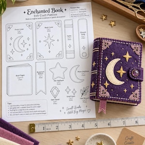 Puede incluir: Una hoja de patrón de fieltro titulada Enchanted Book con diagramas para un adorno de libro, junto a un libro de fieltro morado terminado con una aplicación de luna y estrella, un cierre de gema morada y una cinta métrica de 20 cm.